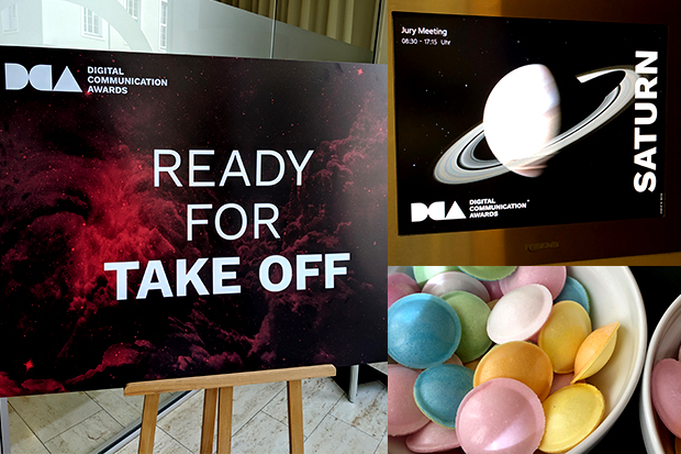 Three images stacked together. In the portrait image on the left, a poster sits on an easel. The poster has the Digital Communications Awards logo in the top left corner and the words Ready For Take Off in front a red and black hued image of swirling star clusters in the cosmos. The top right image features the Digital Communications Awards logo in the bottom left corner, the word Jury Meetings 08:30-17:55 hours in the top left and an image of the planet Saturn in white against a black background. The word Saturn is written horizontal and in white alongside the planet image. The bottom right image is white bowl containing a selection blue, green, pink, yellow and white flying saucer sherbet sweets.