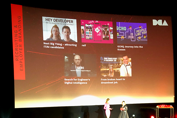 The stage at the Digital Communications Awards 2019 backed by a giant screen listing the 5 shortlisted entrants for the Recruiting and Employer Branding category. The entrants shown are Next Big Thing, Reif, GCHQ Journey into the Known, Search for Engineer’s Digital Intelligence, and From Broken Heart to Dreamboat Job. Two women stand at a podium in front of the screen ready to announce the category winner.