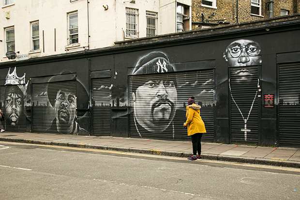 A long black-and-white mural covers an entire wall and several shop shutters. It depicts four iconic musicians. From left to right: Notorious B.I.G., Jam Master J, Big Pun, and Big L.