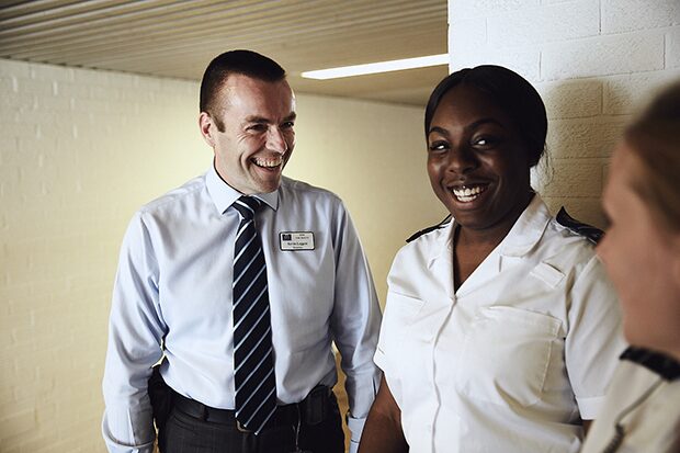 Photo example of a prison governor and two prison officers conversing in a hallway, they are smiling