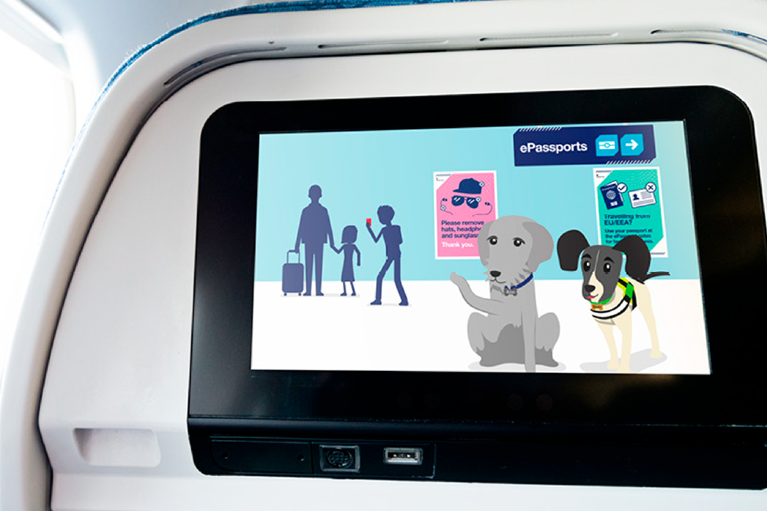 A TV screen on the back of an aeroplane seat is playing a Border Paws video featuring two dog characters teaching children about ePassports